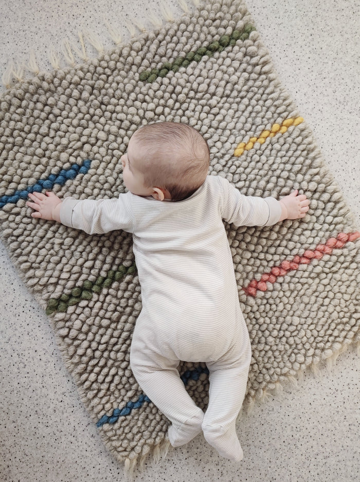 Child playing on the soft woolen Buzhok gray rainbow rug