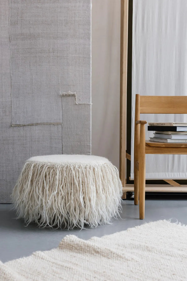 Handcrafted white wool pouf in a contemporary living room, sculptural minimalist accent piece