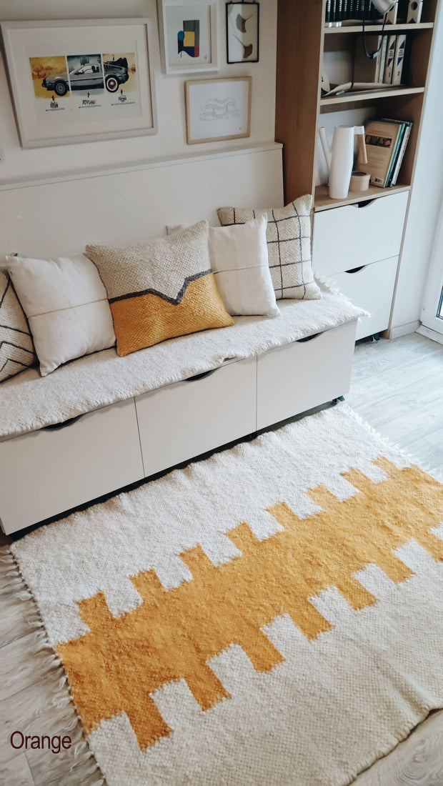 Artisan-made wool rug with bold geometric centerpiece, ivory and orange colorway, evoking Southwestern and tribal textile traditions, old money style