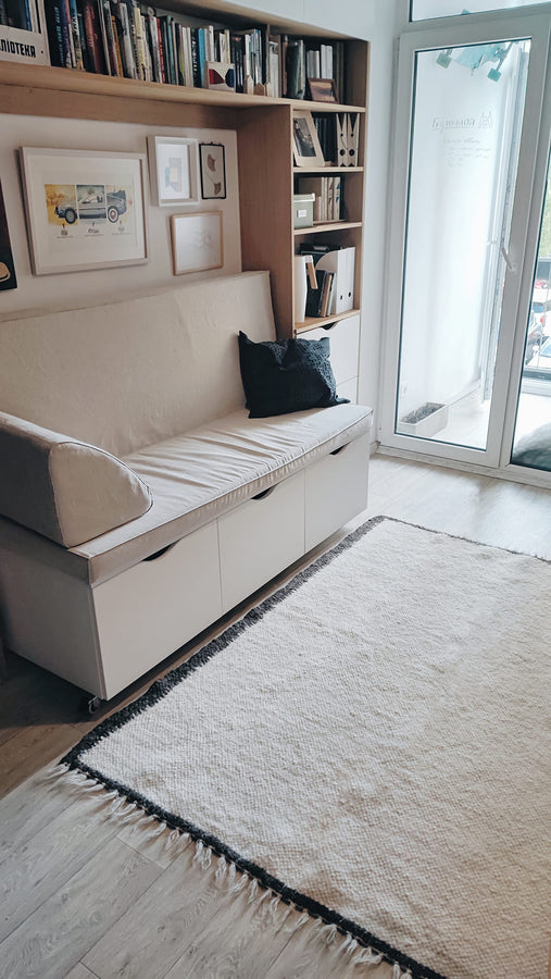 Handmade wool rug in ivory white with black border trim, minimalist Scandinavian-style design