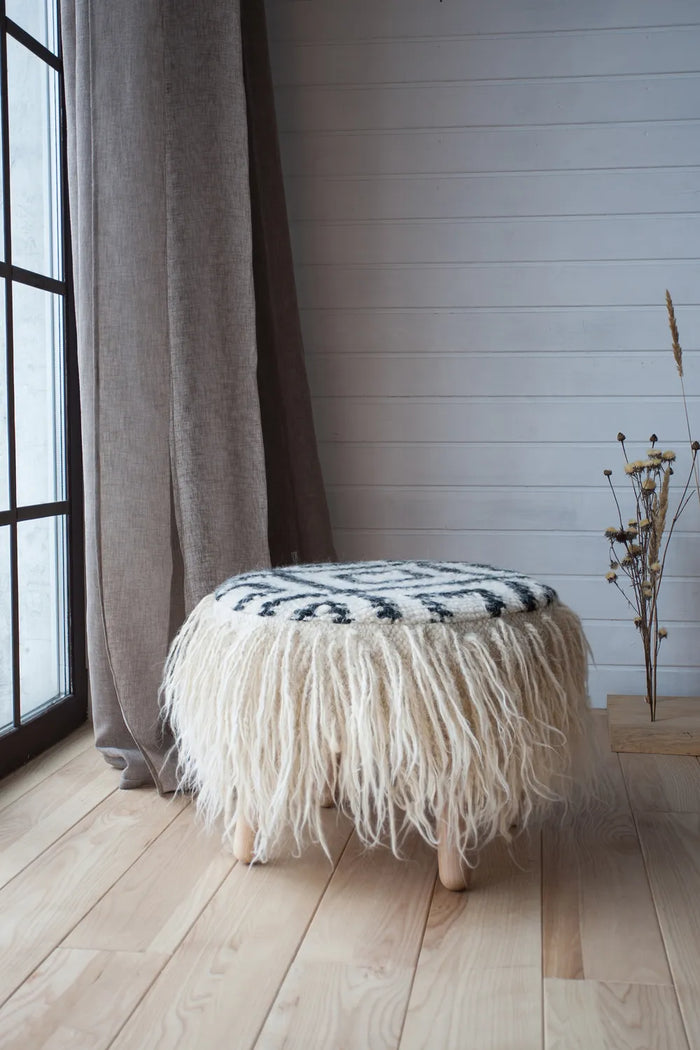 White wool pouf with black ethnic pattern in a cozy living space, traditional Ukrainian-inspired ottoman design