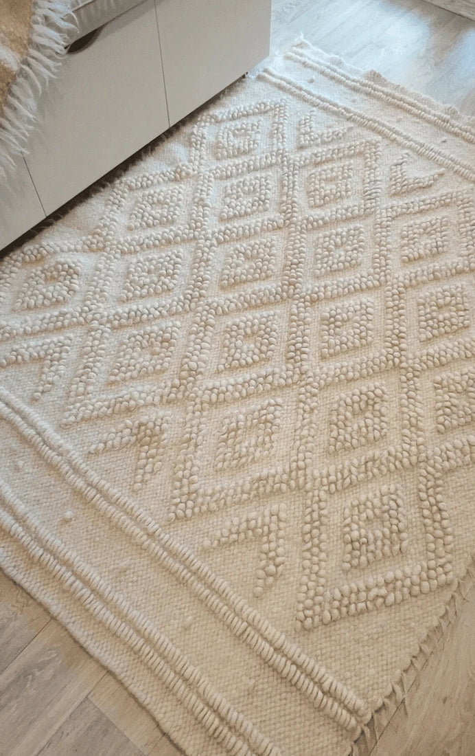 Natural undyed wool rug with raised double-diamond relief texture, monochromatic ivory white design, handcrafted heritage piece