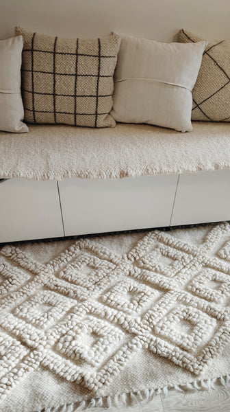 A beige wool rug with a geometric pattern, featuring a herringbone design with fringes on the edges.