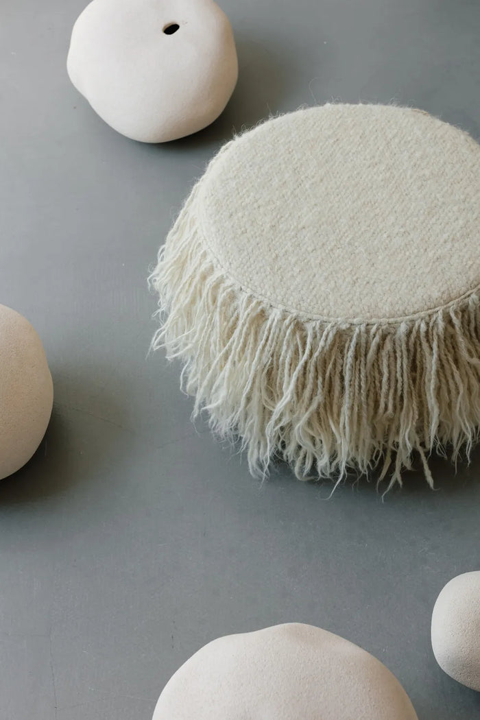 Minimalist wool pouf with elegant hand-stitched seams, natural sheep wool ottoman