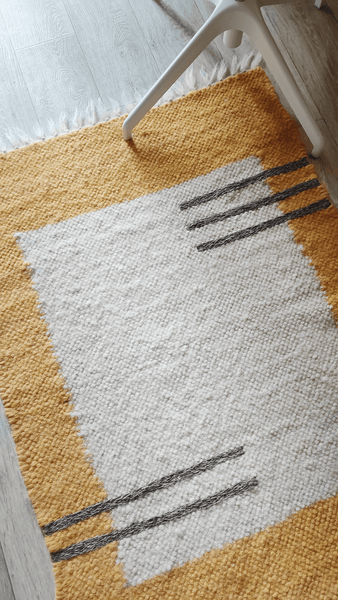 A handcrafted wool rug with a geometric design, featuring a square in the center with a horizontal lines in gray on a ivory white background.