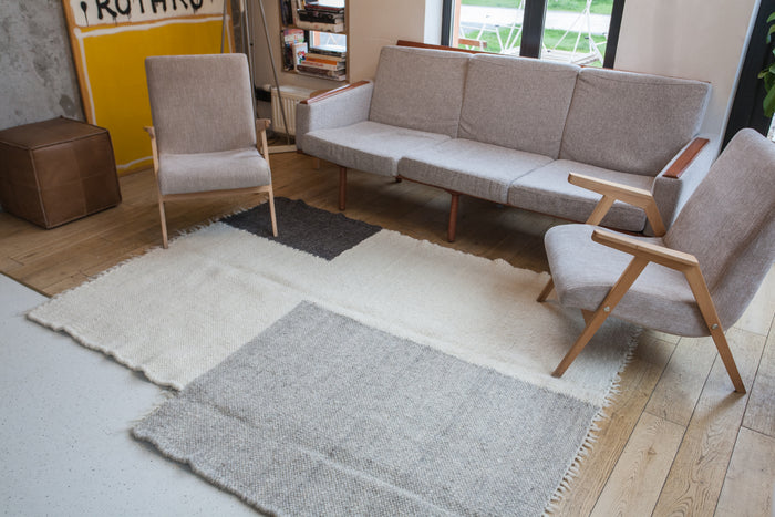 Natural undyed wool rug featuring an asymmetric color-block pattern of ivory, charcoal gray, and soft gray squares