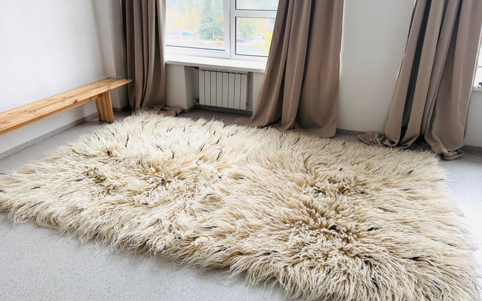 Shaggy flokati wool rug, ivory white base flecked with beige and brown tufts, a cozy minimalist statement piece