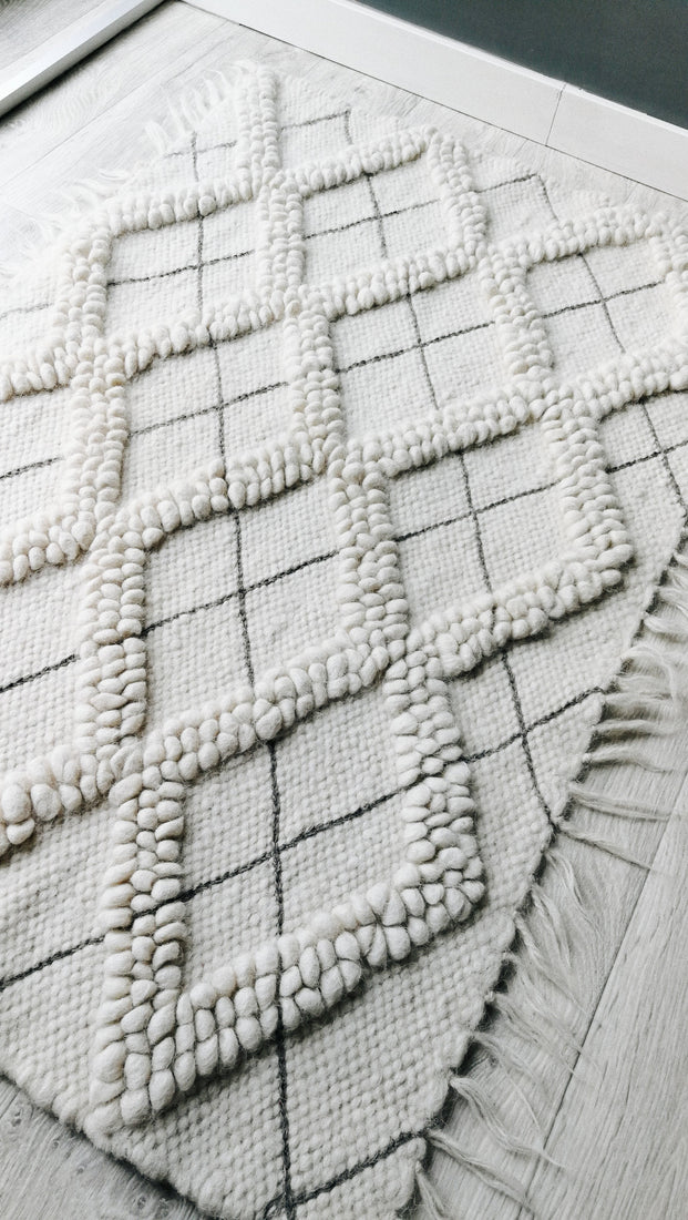 Natural undyed wool rug, all-white diamond motif with tactile looped texture, accented by artisan hand-embroidered geometric details