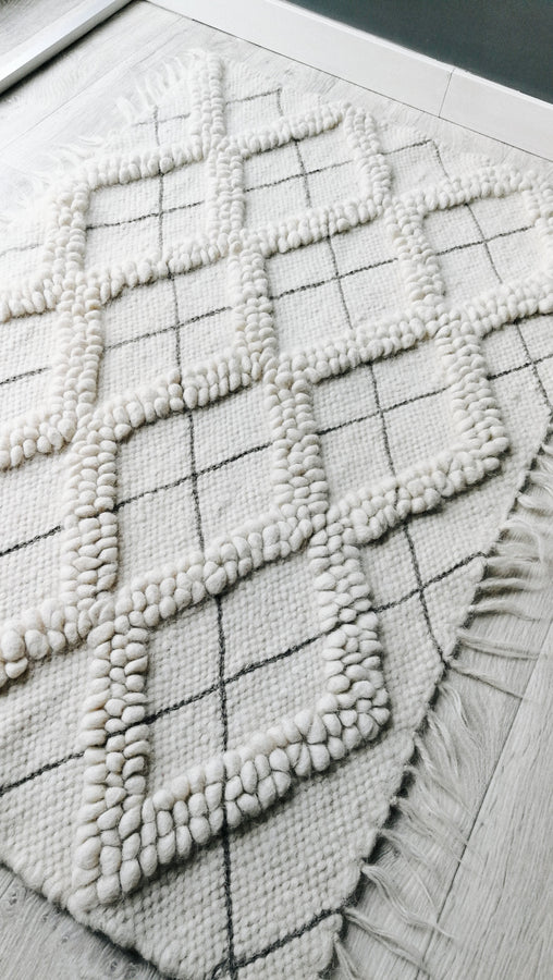 Natural undyed wool rug, all-white diamond motif with tactile looped texture, accented by artisan hand-embroidered geometric details