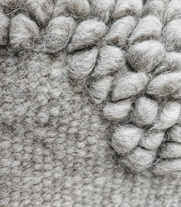 Close-up view of texture sculptural ivory wool rug, diamond-within-diamond motif created through traditional looped weaving, a refined statement piece