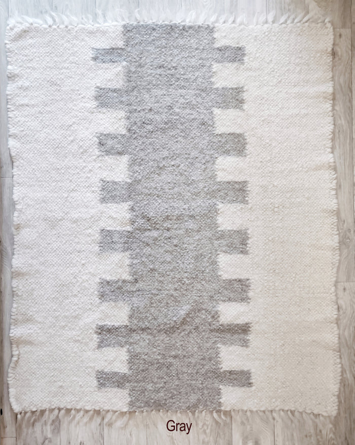 Wool area rug with abstract tribal geometry, ivory white field accented by a central pattern in gray or vibrant orange