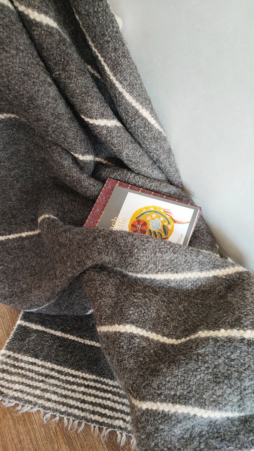 Hand-knotted undyed wool blanket, dark gray base with ivory stripe accents, sustainable home decor