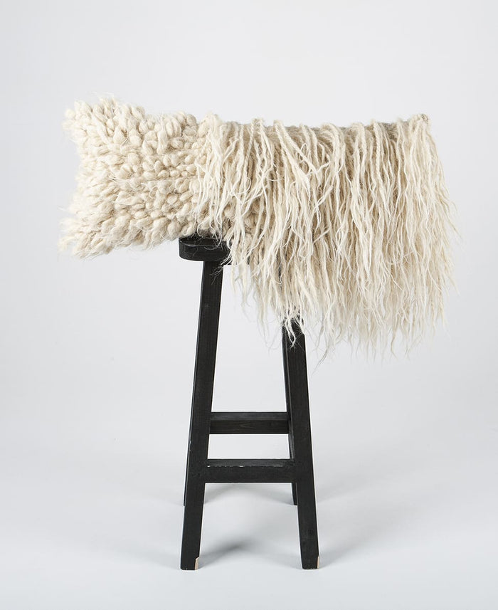 Handmade wool lumbar pillow combining flokati and bobble-knot patterns on the chair