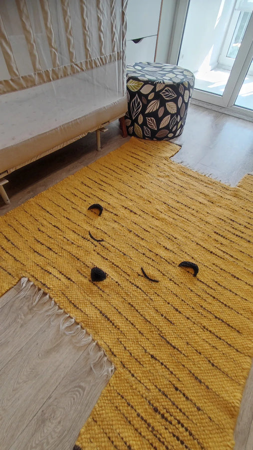 Orange textured rug with black patterns on a wooden floor, next to a bed and ottoman.