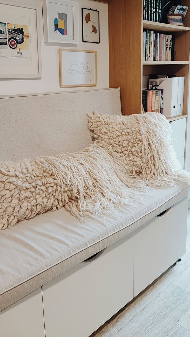 Two wool pillows with bobble and strands on the sofa.